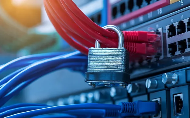 Gros plan sur un cadenas métallique sécurisant des câbles réseau rouges branchés sur un commutateur (switch) informatique, symbolisant la cybersécurité et la protection des données.