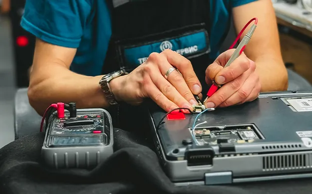 Technicien effectuant la maintenance d'un ordinateur avec un multimètre.